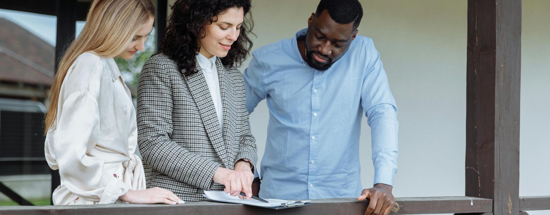 Real estate agent discussing property paperwork with a couple on a porch.
